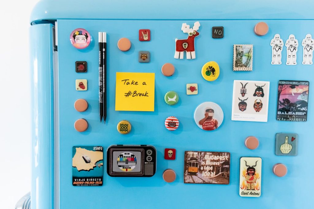 A vibrant collection of magnets on a blue fridge, featuring souvenirs and a sticky note reading Take a #Break.